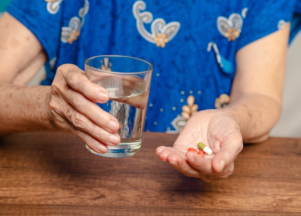 Mujer mayor toma pastillas con un vaso de agua.