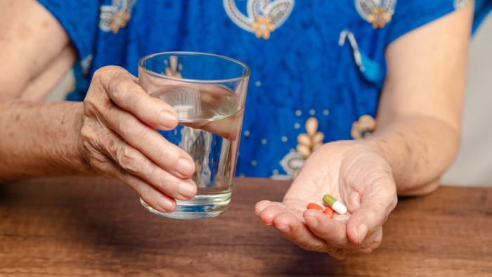 Mujer mayor toma pastillas con un vaso de agua.